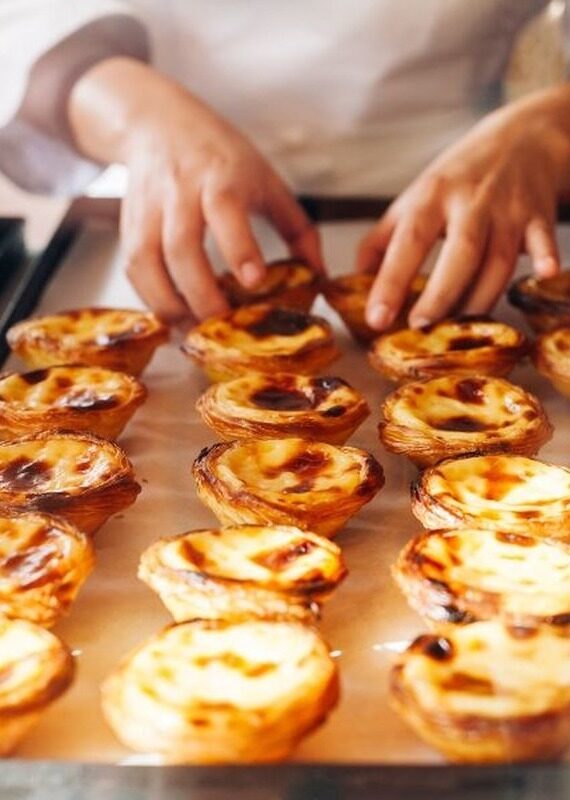 A person in a white chef's coat arranges a tray of freshly baked custard tarts with caramelized tops.