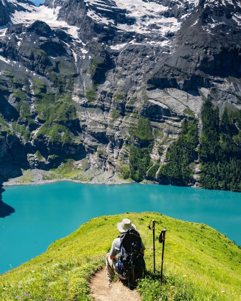 Switzerland travel – Senior man hiking looking at the scenic views high above the Oeschinen lake in the Swiss Alps near Kandersteg. Popular hiking around the turquoise-colored lake with majestic views of waterfalls and lake