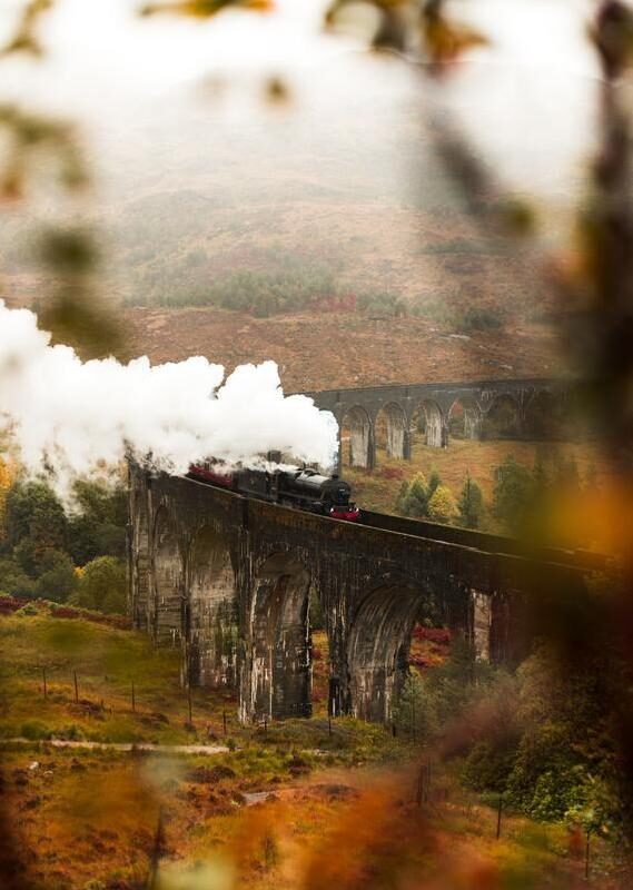 A steam train crosses a high stone viaduct in a misty, expansive, autumn landscape, an iconic view of luxury Europe rail tours.