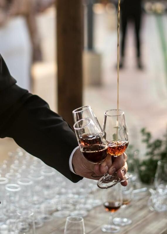 Close-up of a hand holding three glasses while a stream of amber liquid is poured into one from above.