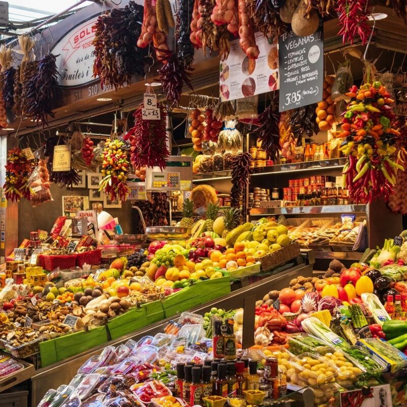 A market display filled with piles of citrus, tropical fruits, and long strings of dried red peppers hanging.