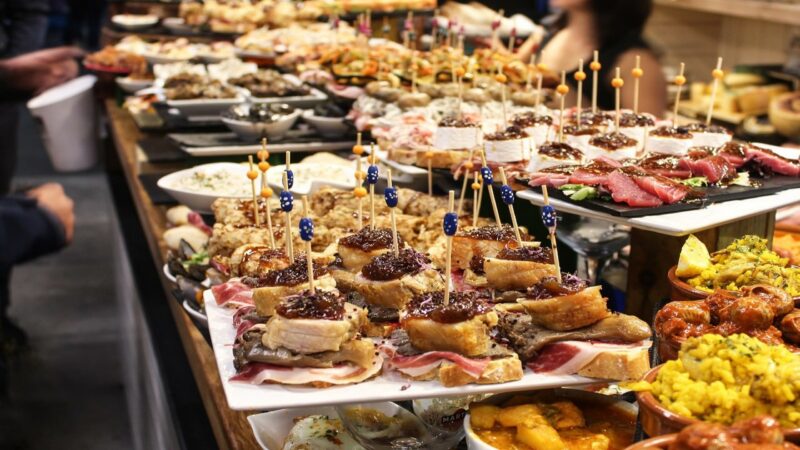 A long counter filled with various small appetizers on bread, held together with toothpicks, including tuna and ham.