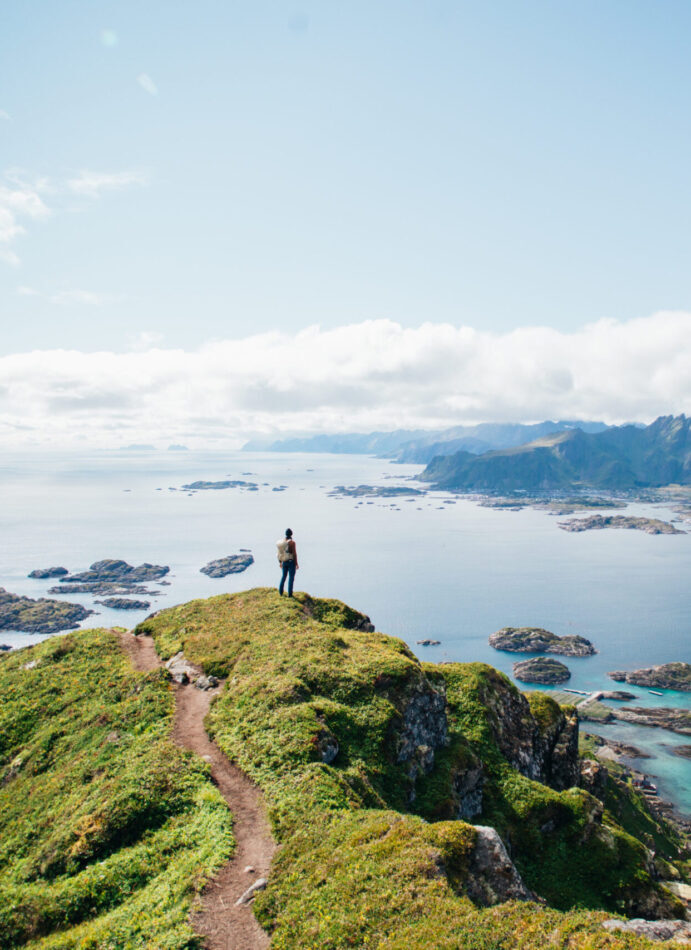 Amazing epic shot of young man hiker stand on top of mountain after long difficult hike in Lofoten Islands in Norway. Incredible summer views of scandinavian travel lifestyle. Epic landscape in north