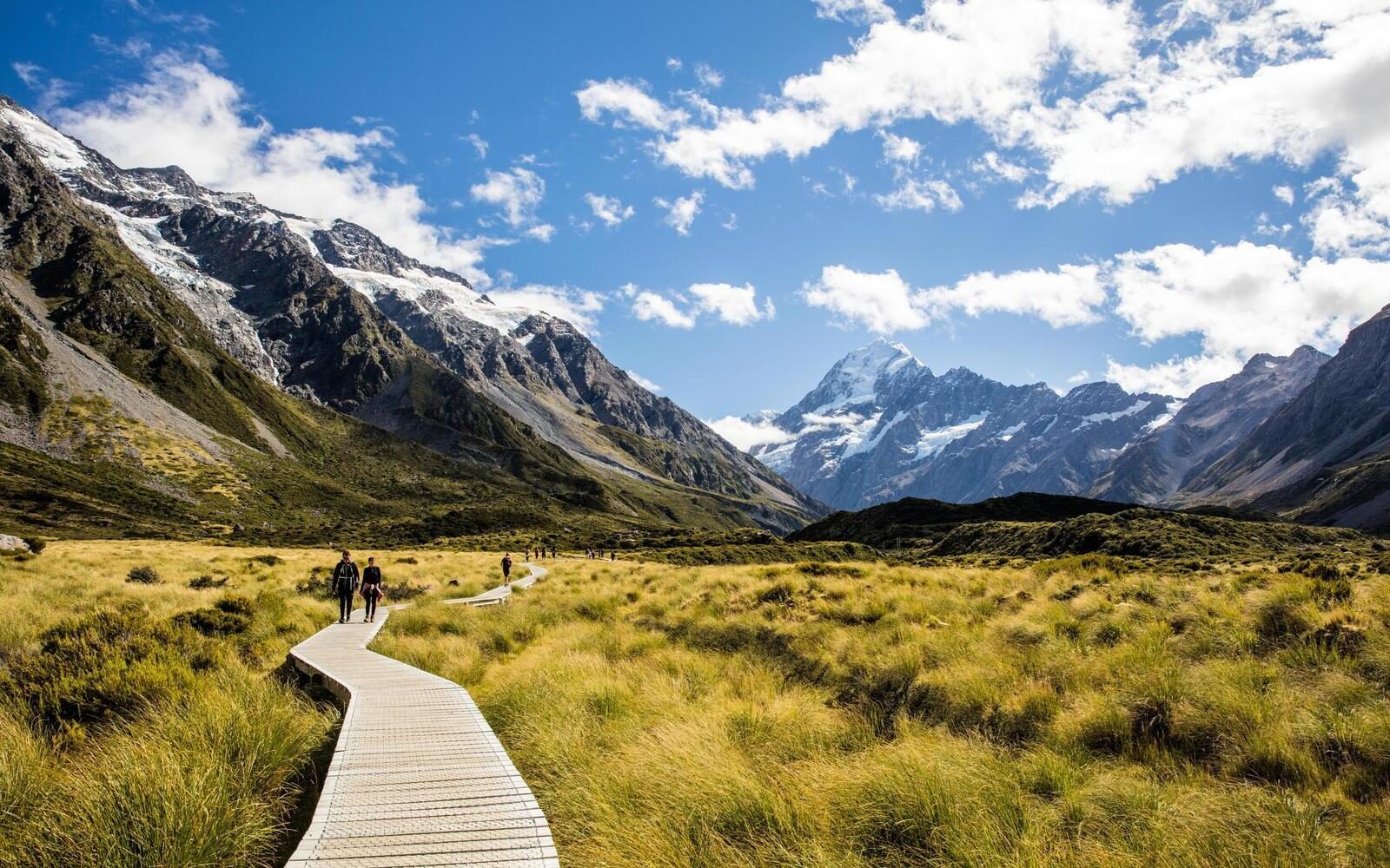 An open boardwalk winding through Mount Cook National Park beneath the snow-capped peak of Aoraki in New Zealand.