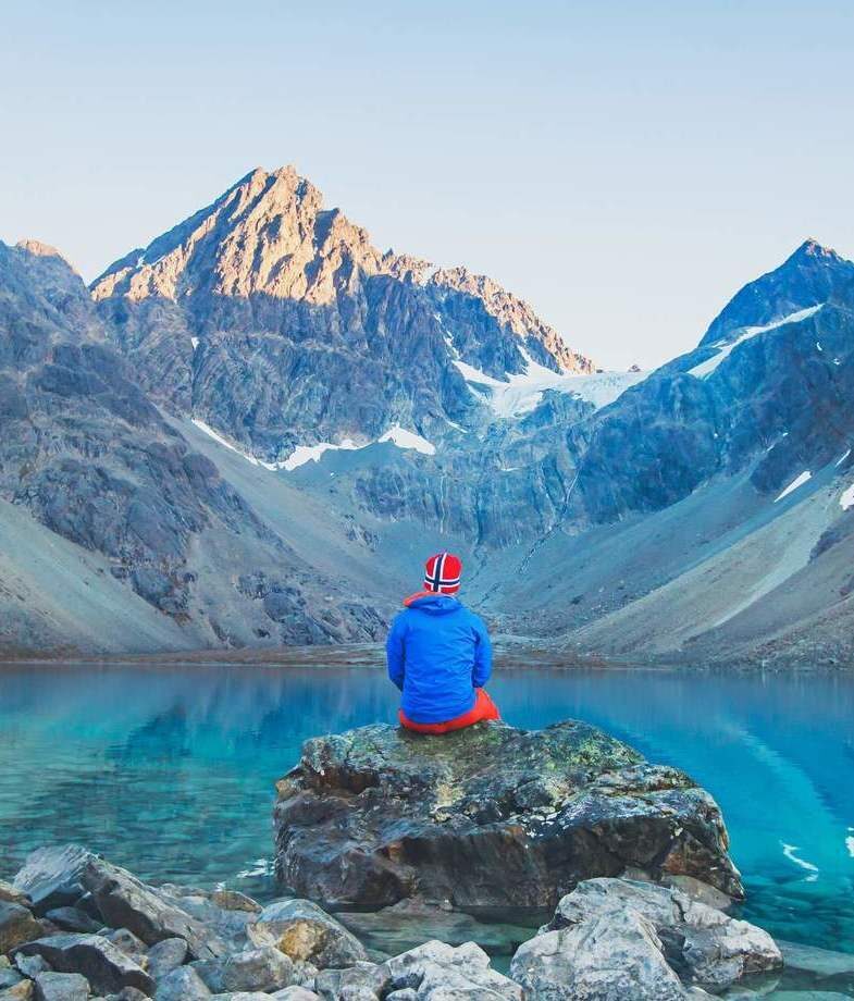 The glacial Blue Lake of Blavatnet with views of the Lyngen Alps in northern Norway and the hilltop Gergeti Trinity Church in Kazbegi National Park, Georgia.
