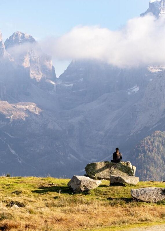 A person meditating on a rock in front of misty, jagged mountains for a positive impact.