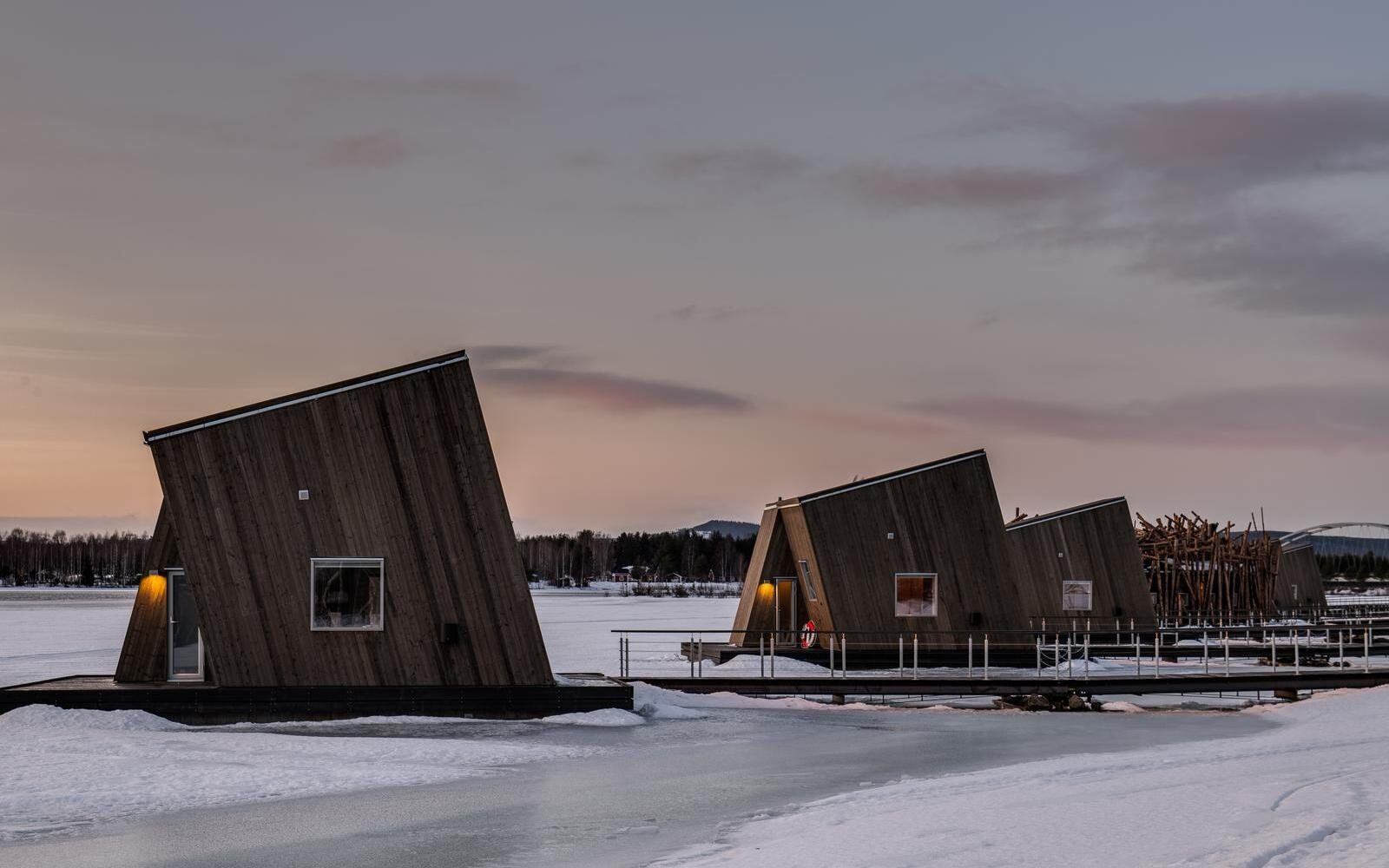 The floating wooden cabins of Arctic Bath in Sweden resting on a frozen river under soft winter light.