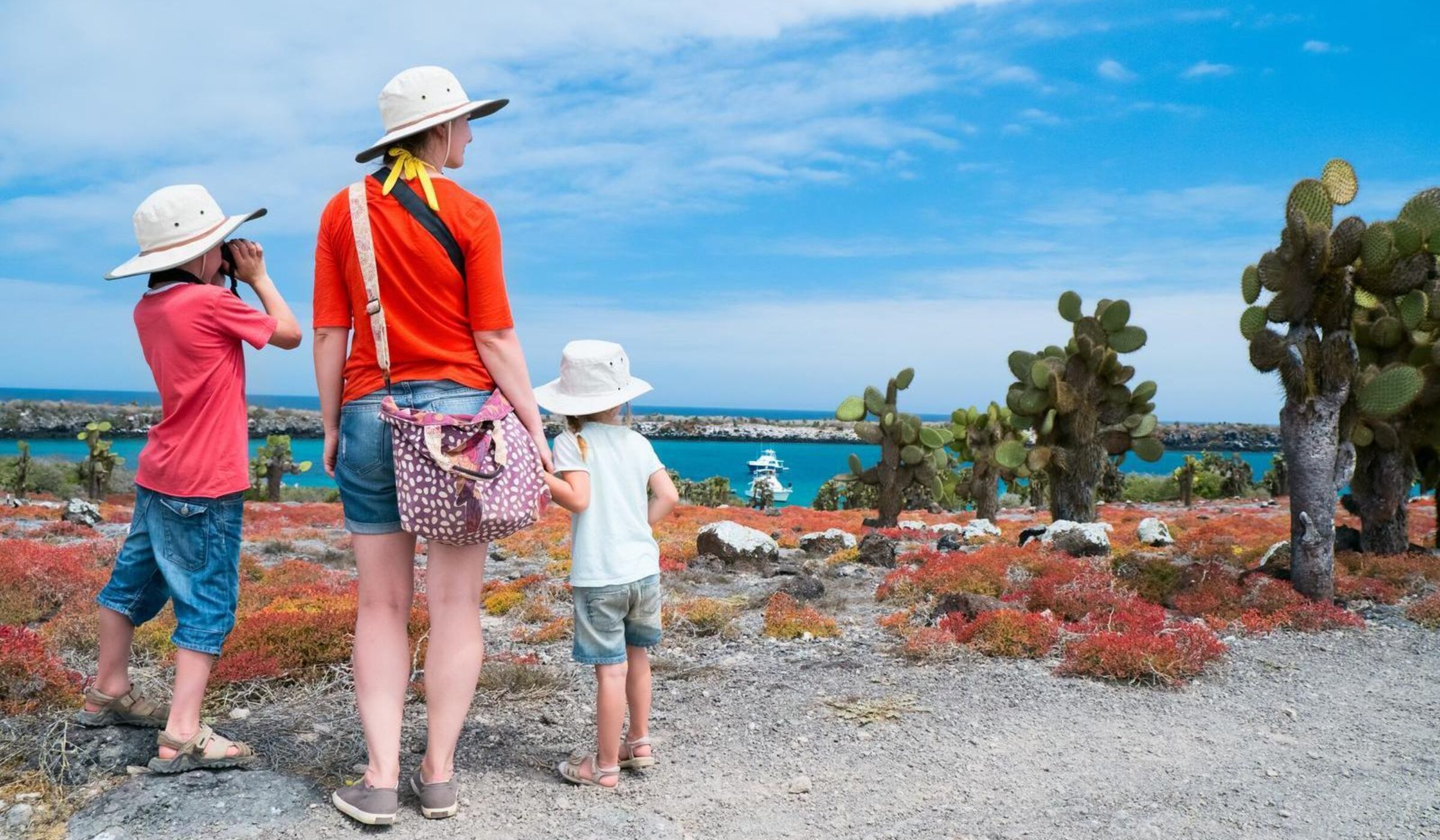 A mother and two children looking out over cacti and turquoise waters on a Galápagos island landing.