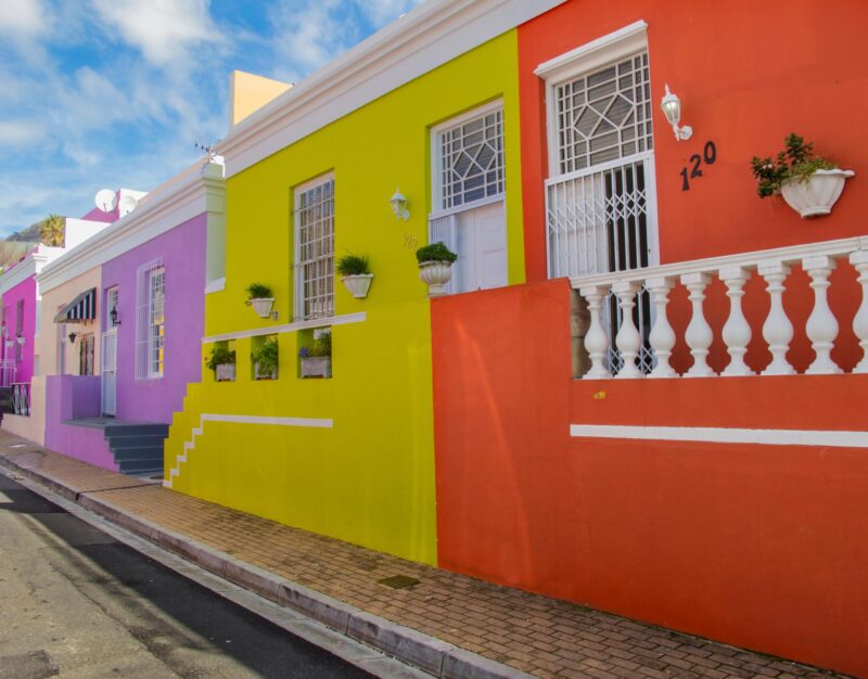 Brightly painted yellow, orange, and purple houses on a street during luxury Cape Town trips.