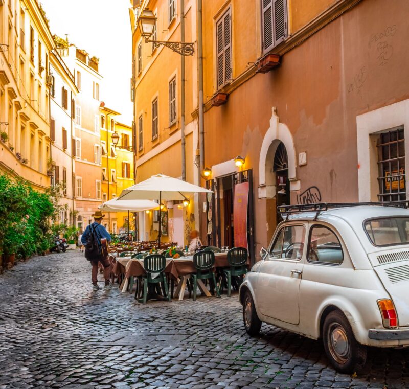 A vintage Fiat 500 sits parked beside a cafe in Trastevere, Rome.