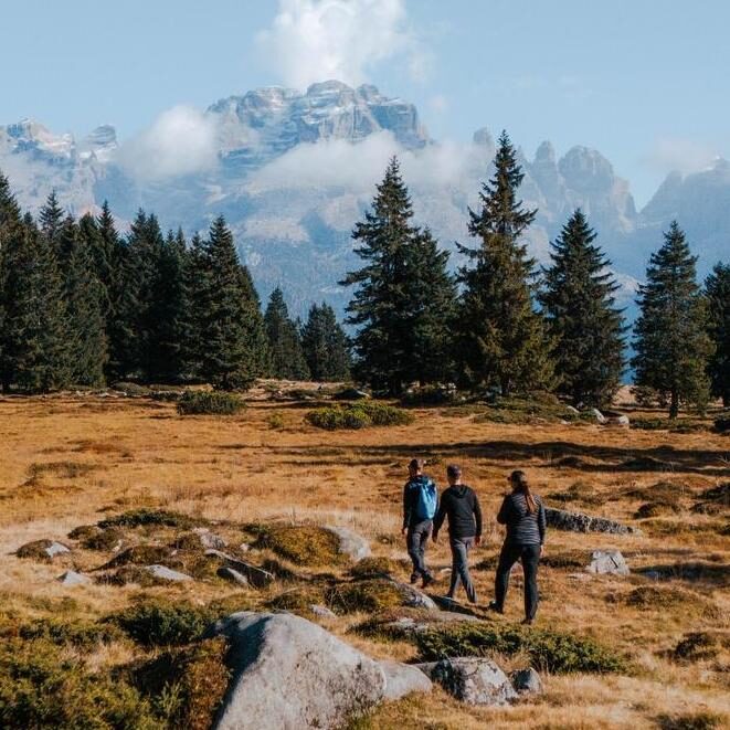 Three people hiking in Italy with the Dolomites in the background.