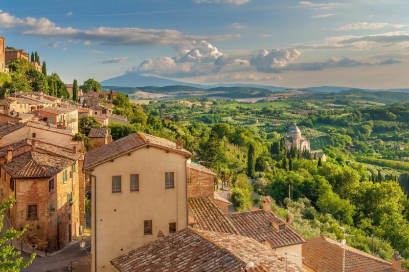 View over terracotta rooftops of a hillside town toward a green valley and mountains, featuring luxury Tuscany trips.