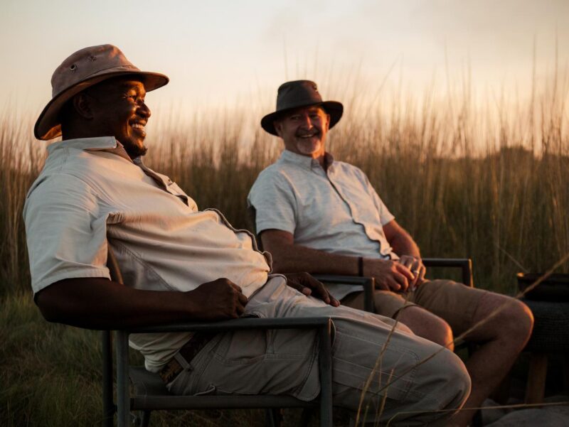 Two men sitting and smiling at sunset for a positive impact.