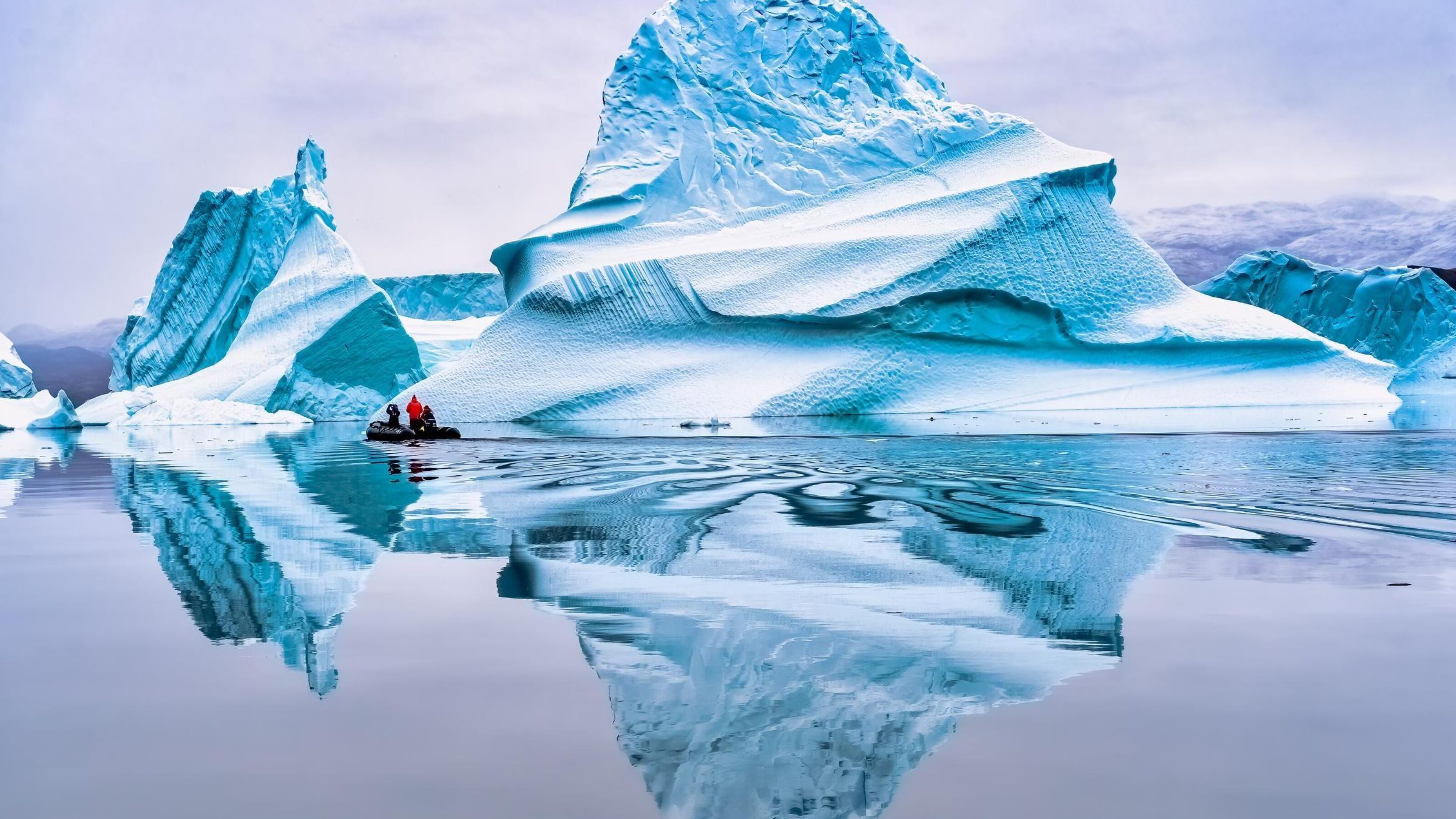 A zodiac boat in the distance up close to an iceberg in the sea at Scoresby Sound in Greenland