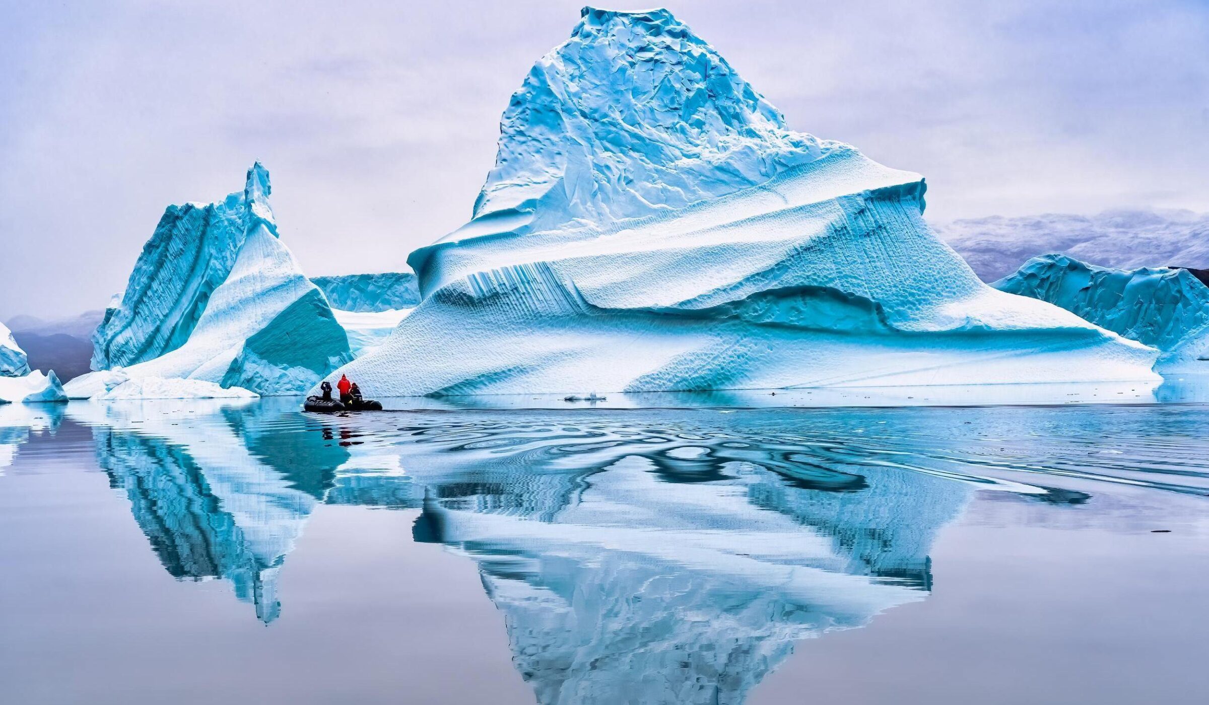A group of people on a Zodiac cruising past a giant iceberg.