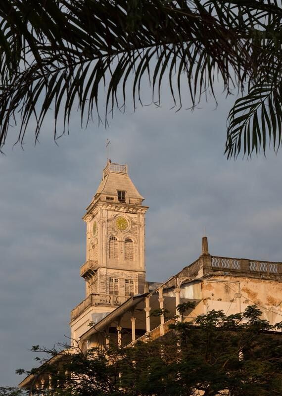 Beit-al-Ajaib (House of wonders) in Zanzibar Stone town. Lit up with sunlight and framed with foliage.