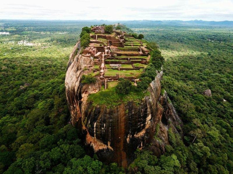 The ancient Sigiriya Rock fortress, a UNESCO World Heritage site in Sri Lanka, towering over lush tropical jungles under a clear sky.