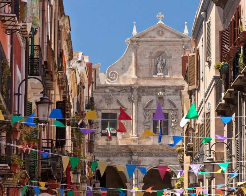 Colourful flags strung up between houses with a Baroque church in the background in Cagliari, Sardinia