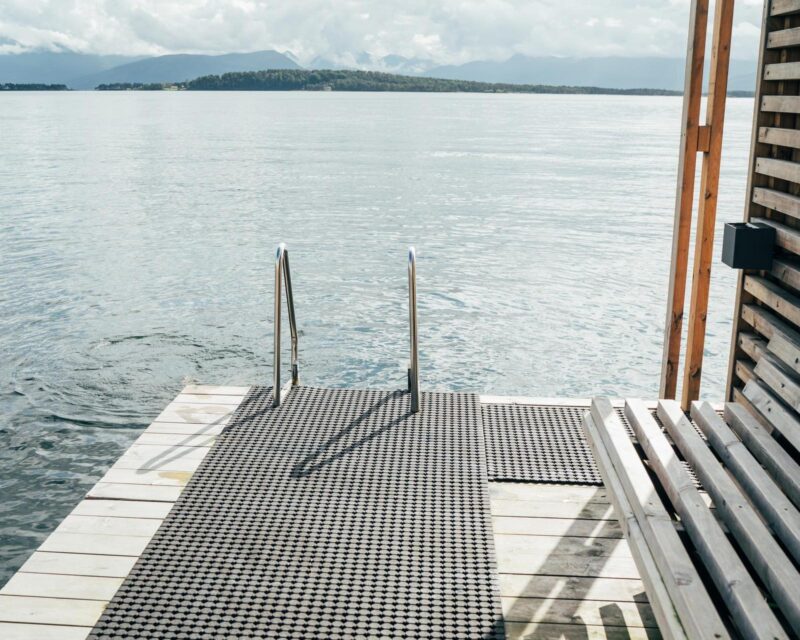 Norwegian floating sauna features in Scandinavian minimalism design with wooden deck over calm waters of Molde Fjord.