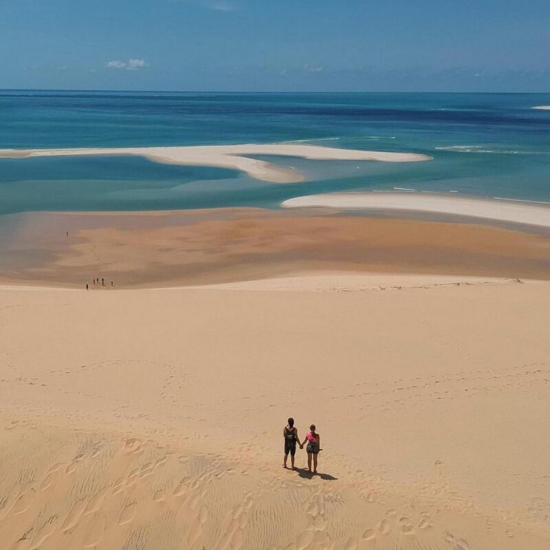 A couple overlooks a vast beach and turquoise ocean from a high sand dune in the Bazaruto Archipelago.