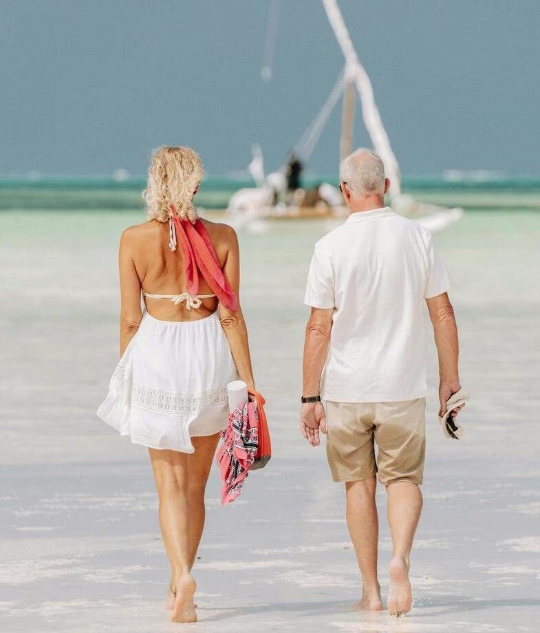 A couple walking barefoot along the white sands of a Zanzibar beach toward a dhow boat, and a traditional mokoro safari gliding through the calm waters of the Okavango Delta.