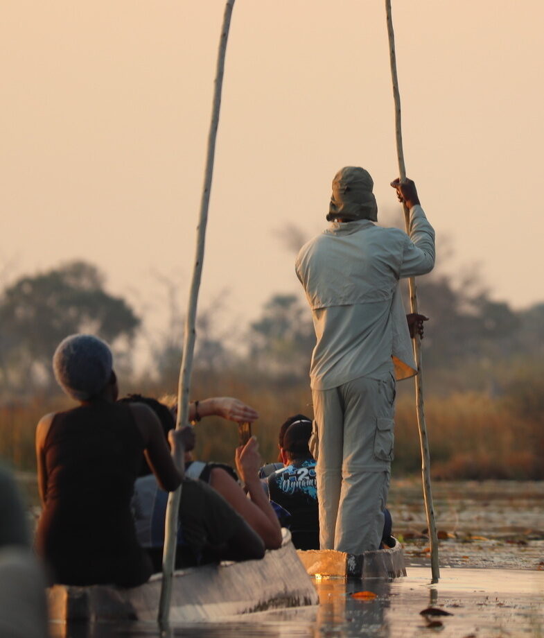 A couple walking barefoot along the white sands of a Zanzibar beach toward a dhow boat, and a traditional mokoro safari gliding through the calm waters of the Okavango Delta.