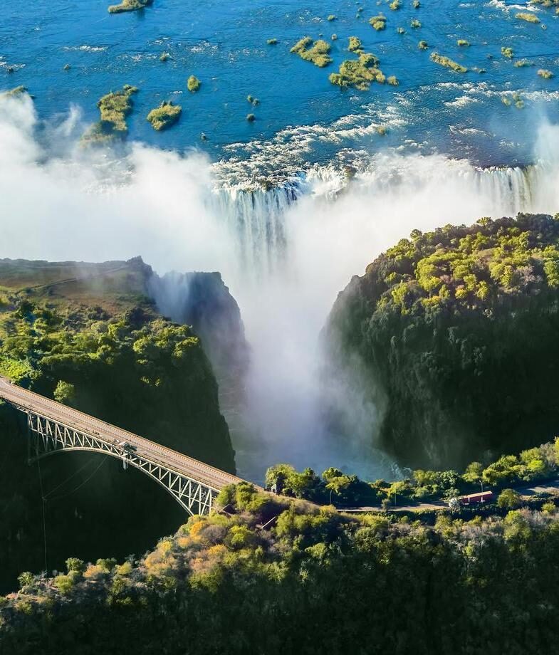 A herd of elephants gathering to drink at a watering hole in Etosha National Park, and the immense cascade of Victoria Falls, where rising mist can reveal a rainbow on a lucky day.