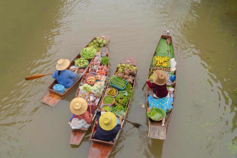 Overhead view of vendors in wooden boats filled with colourful produce on a Bangkok canal.