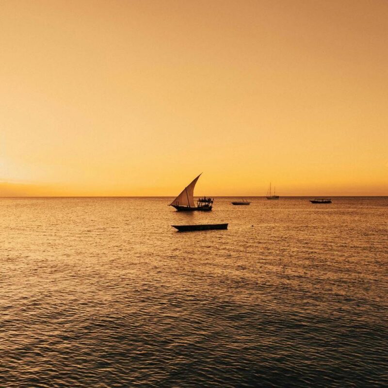 A silhouette of a dhow sailboat on the ocean at sunset in Zanzibar.