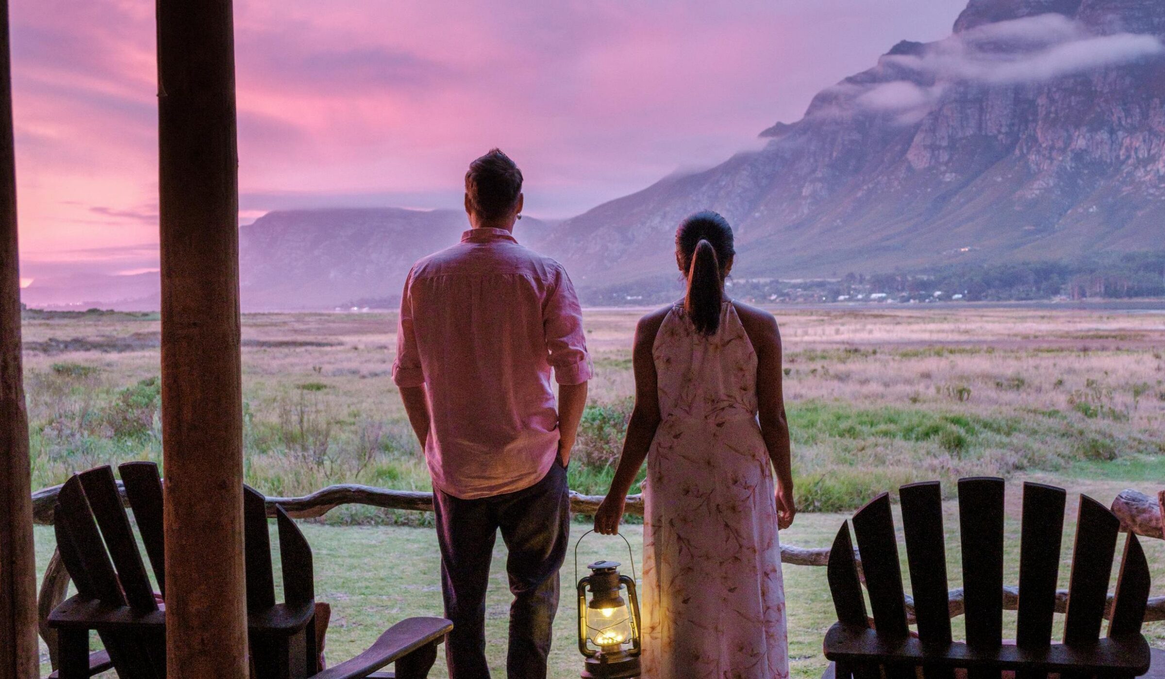 A couple looks out at a mountain landscape during a pink and purple sunset on the Whale Coast of South Africa.