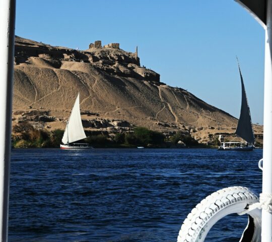 Drifting along the Nile River by traditional felucca, sailing past golden desert hills and ancient riverside temples
