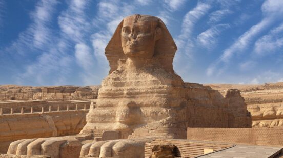 Front view of the Great Sphinx of Giza in Egypt with desert landscapes and a blue sky in the background.