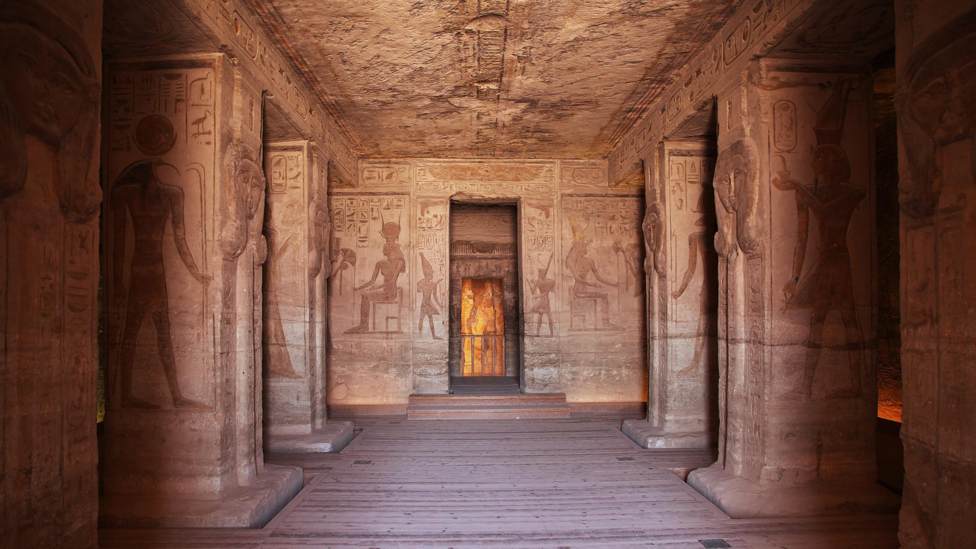 The interior of an ancient Egyptian temple featuring large stone pillars and walls covered in detailed carvings.