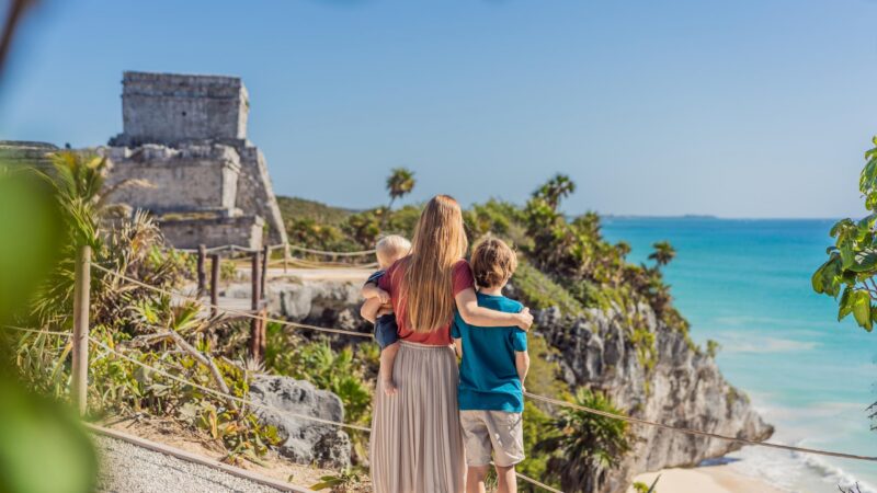 Family stands at Tulum ruins overlooking the ocean during a Mexico family vacation.