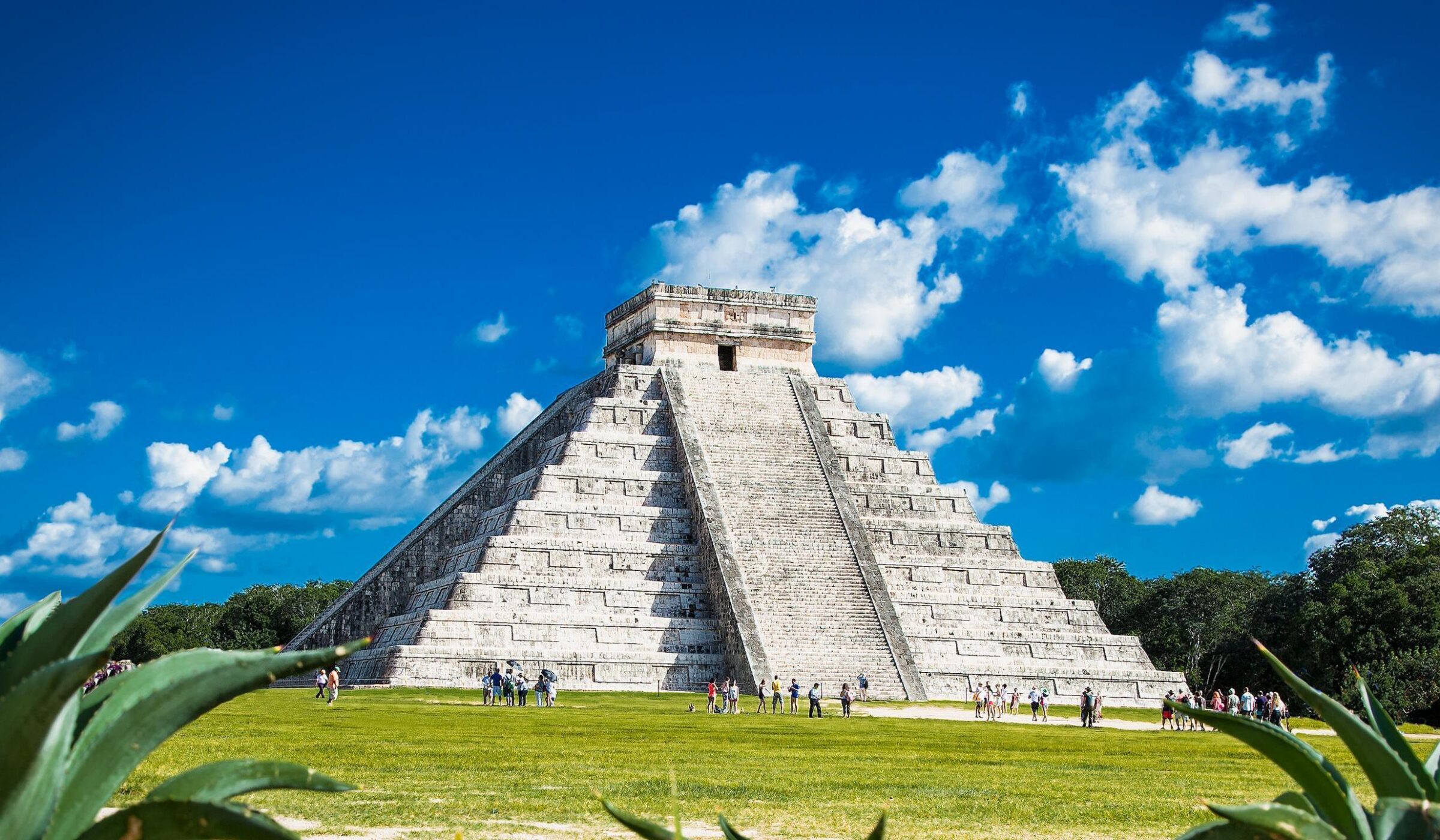 The ancient Mayan pyramid of Chichen Itza in Mexico surrounded by green grass and visitors.