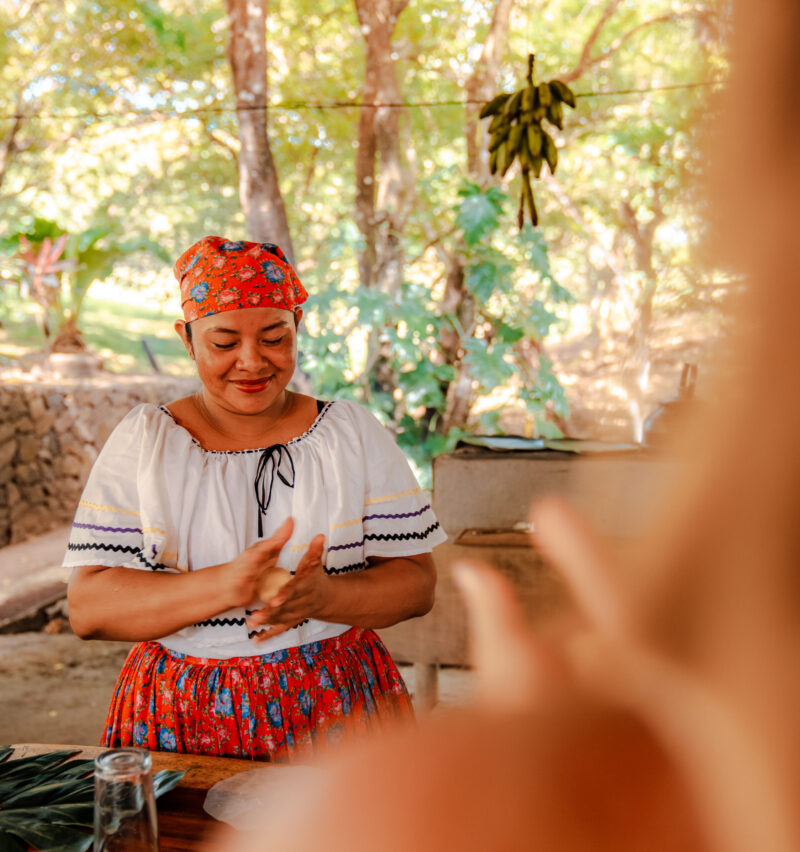 A woman in traditional Guanacaste dress rolls a tortilla and smiles during a cooking class.