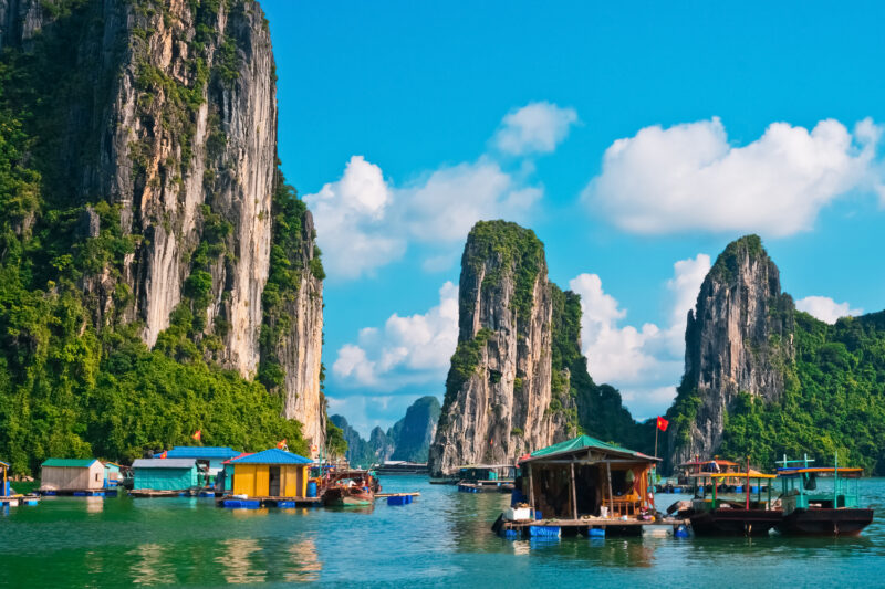 Brightly colored floating houses and boats in Halong Bay, Vietnam, with massive limestone cliffs in the background.