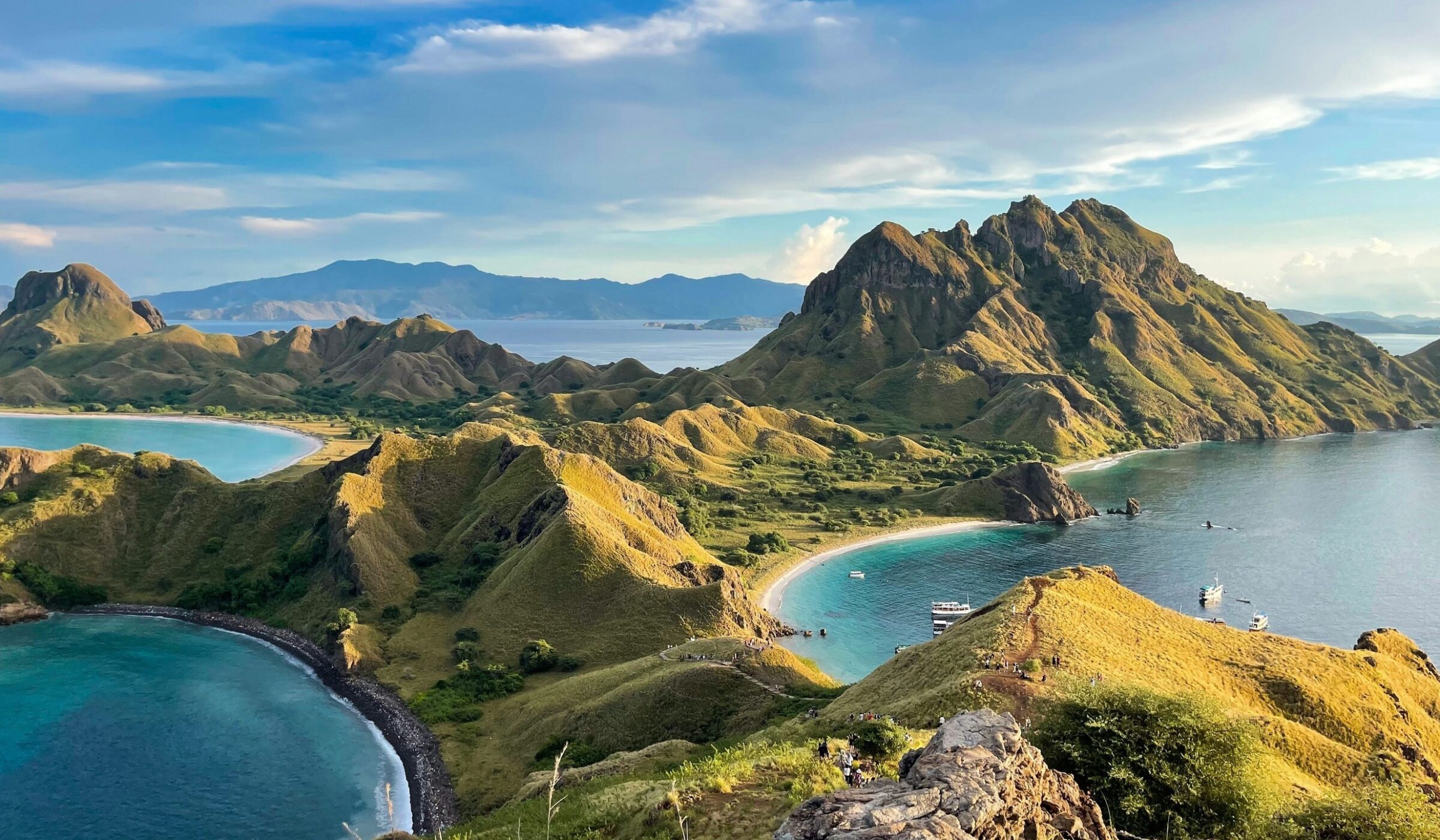 Landscape view of Padar Island with rolling green hills and multiple blue ocean bays under a cloudy sky.