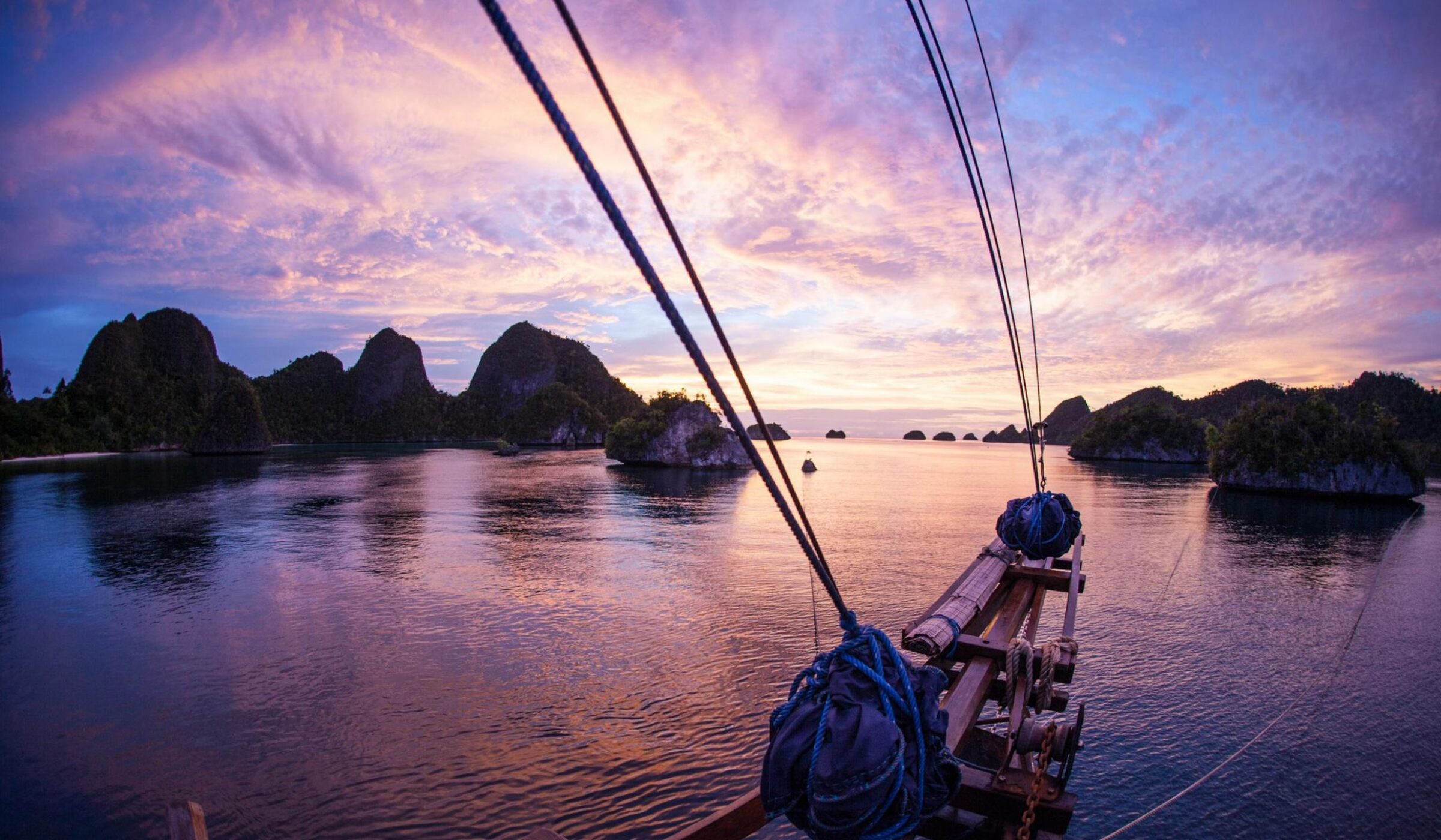 View from the front of a wooden boat looking out at a purple sunset over tropical islands.