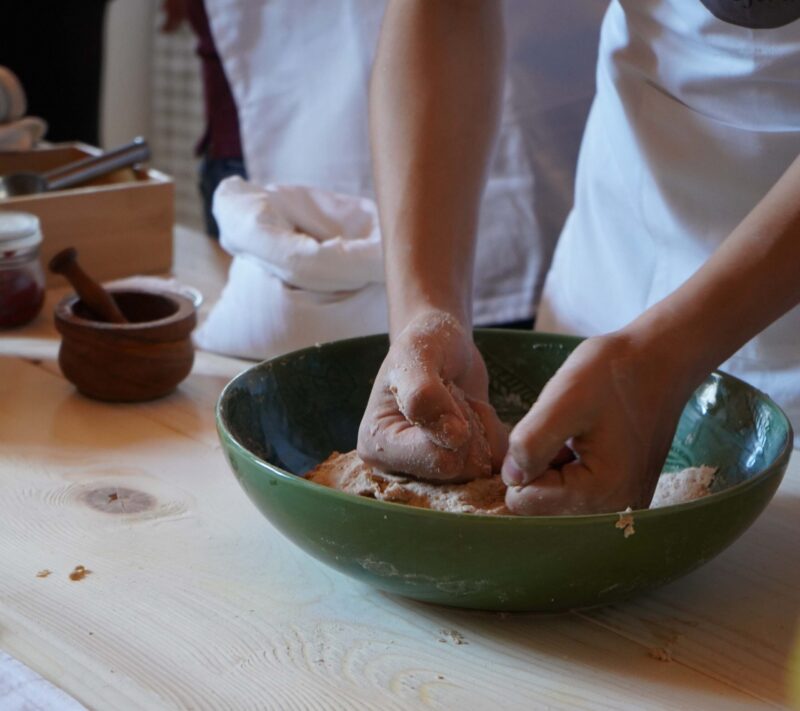 A child’s hands kneading dough in a green ceramic bowl during