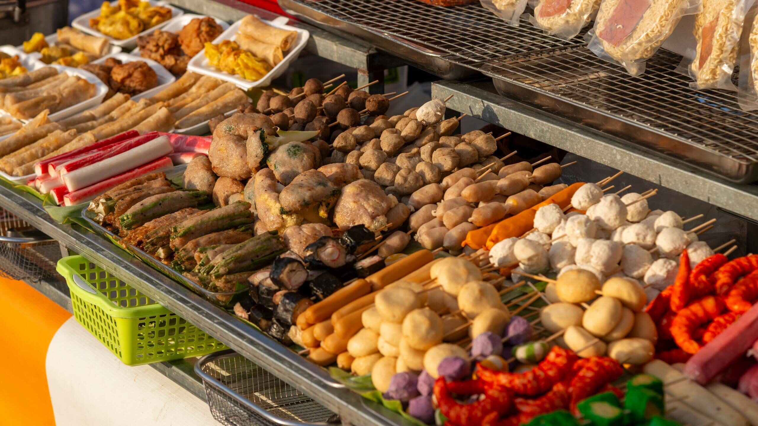 A variety of grilled meat skewers, fish balls, and fried snacks displayed on a street food stall in Phnom Penh.