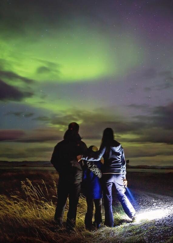 Family silhouette looking at the green northern lights in a night sky during an Iceland family luxury tour.