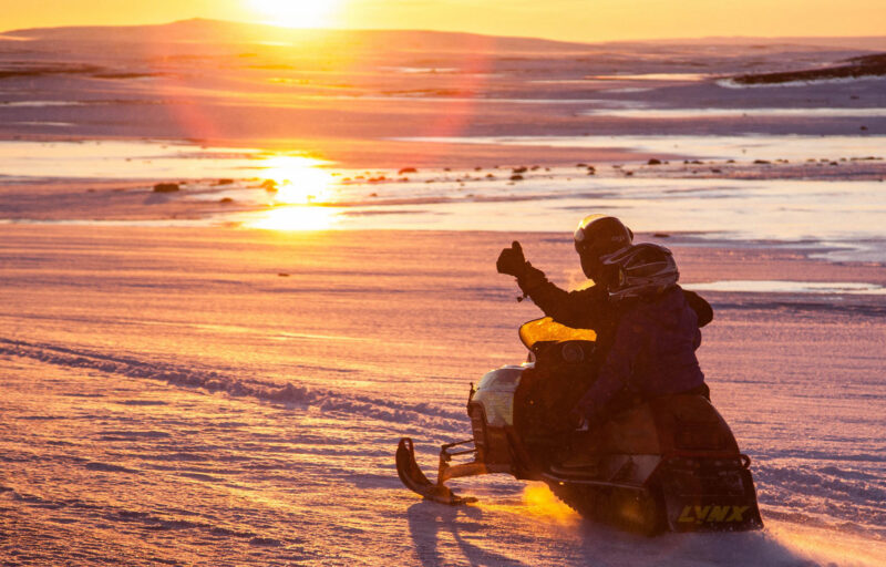 Two people riding a snowmobile on a snowy field at sunset during an Iceland family luxury tour.