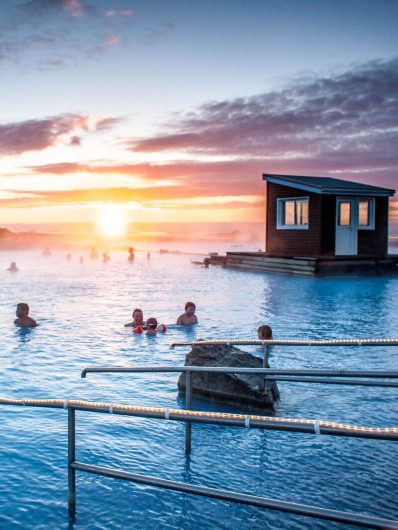People swimming in a geothermal spa at sunset during an Iceland family luxury tour.