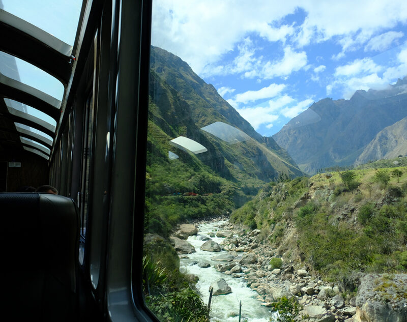 A view of a river and mountains from a glass-roofed car on luxury Peru train vacations.
