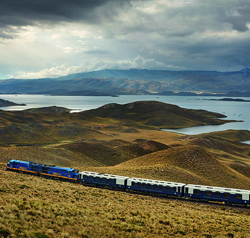 A train traveling through hills past a lake on luxury Peru train journeys.