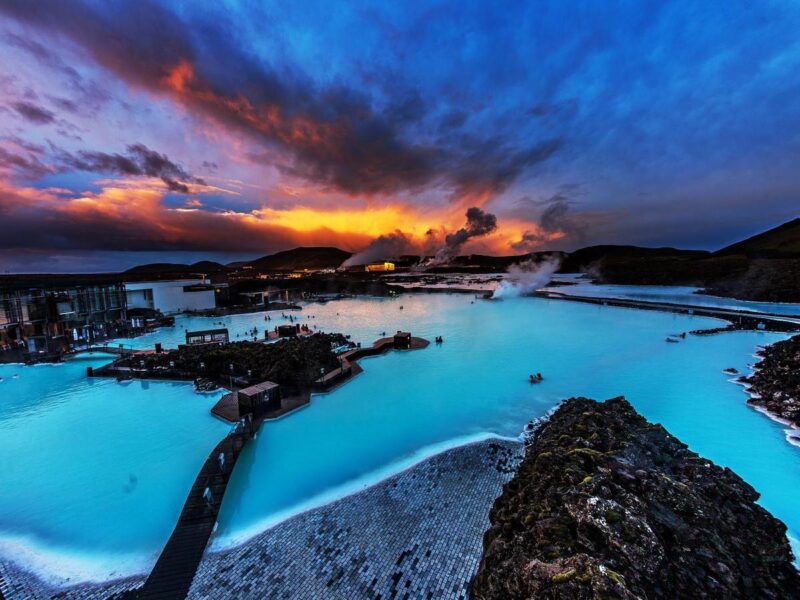 Geothermal spa with milky blue water and rising steam under a vibrant orange and purple sunset sky in Iceland.