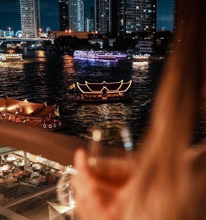 View of Chao Praya river in Bangkok as a woman looks on with a drink from her balcony.