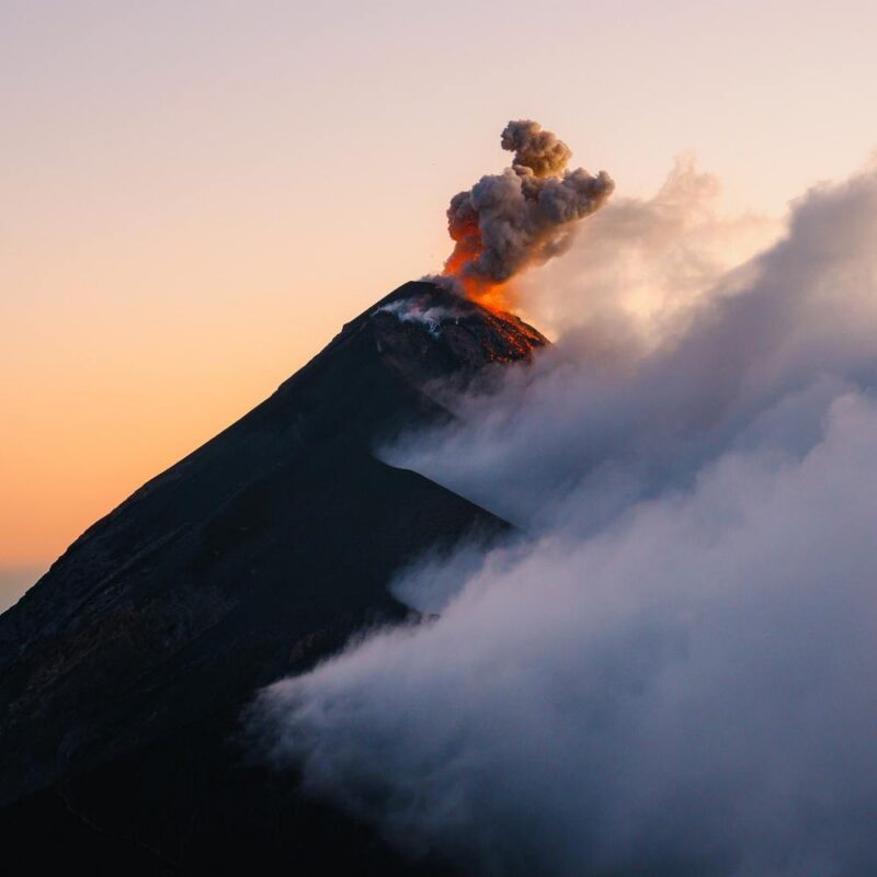 A view of an erupting volcano at sunrise half covered with cloud