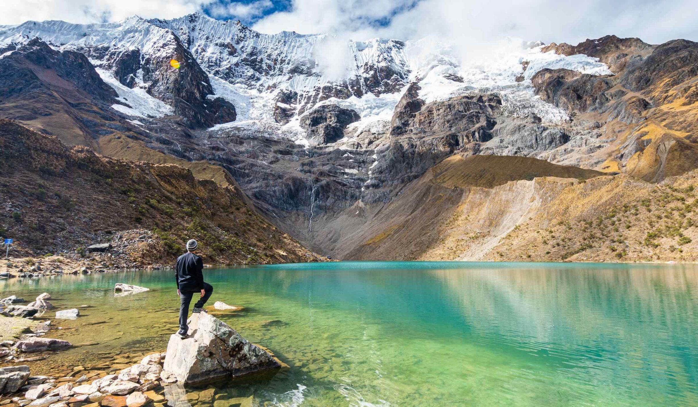 A hiker stands at the edge of Lake Humantay in Peru admiring the view